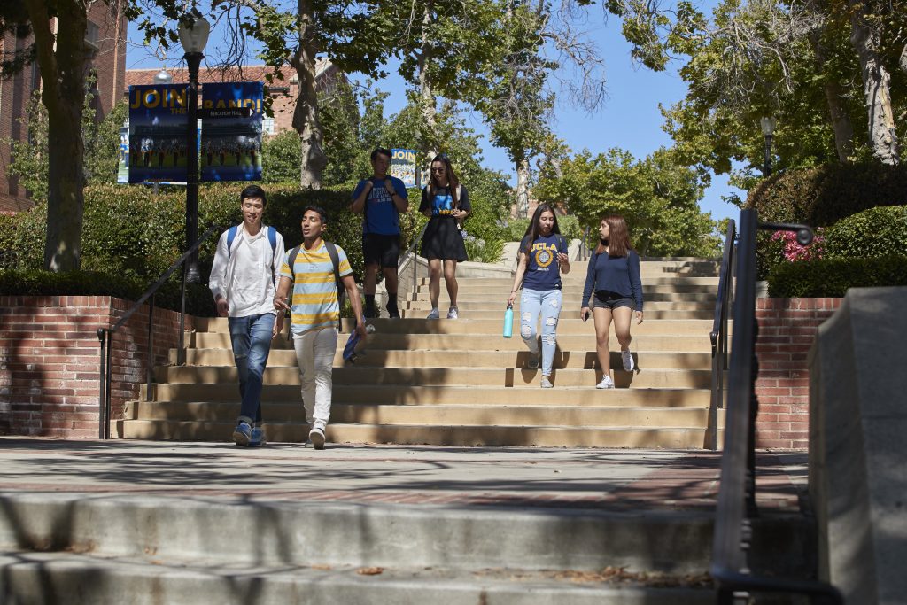 Six students talk to each other and walk down steps on the UCLA campus.